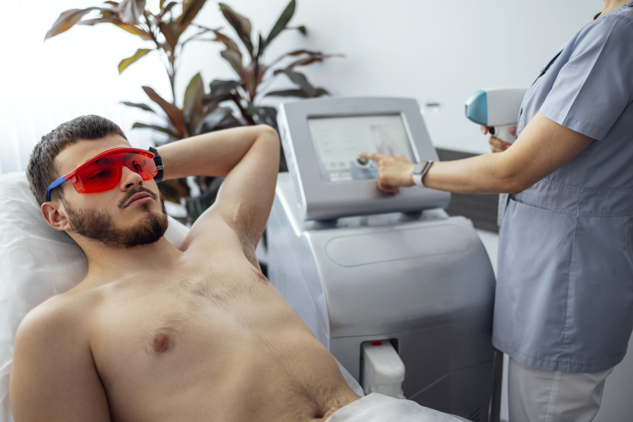 Young man receiving photo epilation while visiting beauty center on salon, professional female beautician doing laser hair removal procedure on clients face. Cosmetology concept